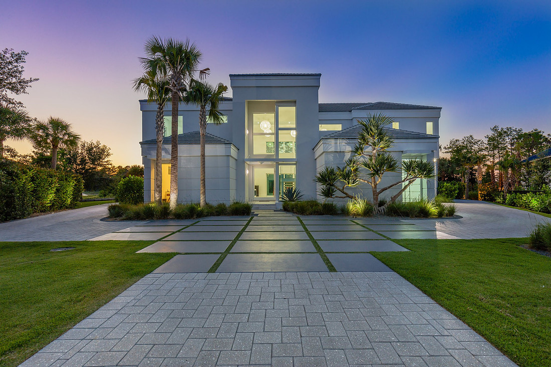 Modern luxury home front entrance at twilight with palm trees and landscape lighting in Florida