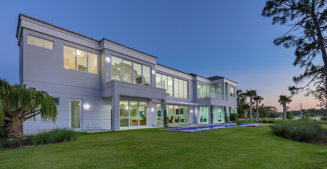 Modern two-story luxury home rear exterior at twilight with glowing windows and pool in Florida