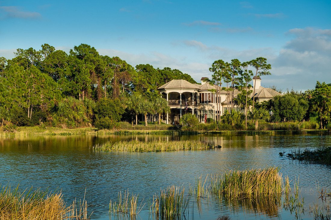 Lakefront estate home among pine and palm trees reflected in a calm Florida lake