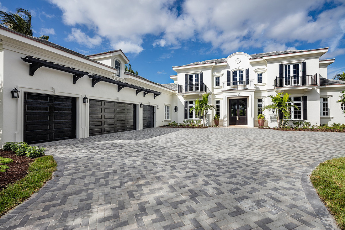 White luxury home with black shutters, iron balconies, three-car garage and herringbone paver driveway