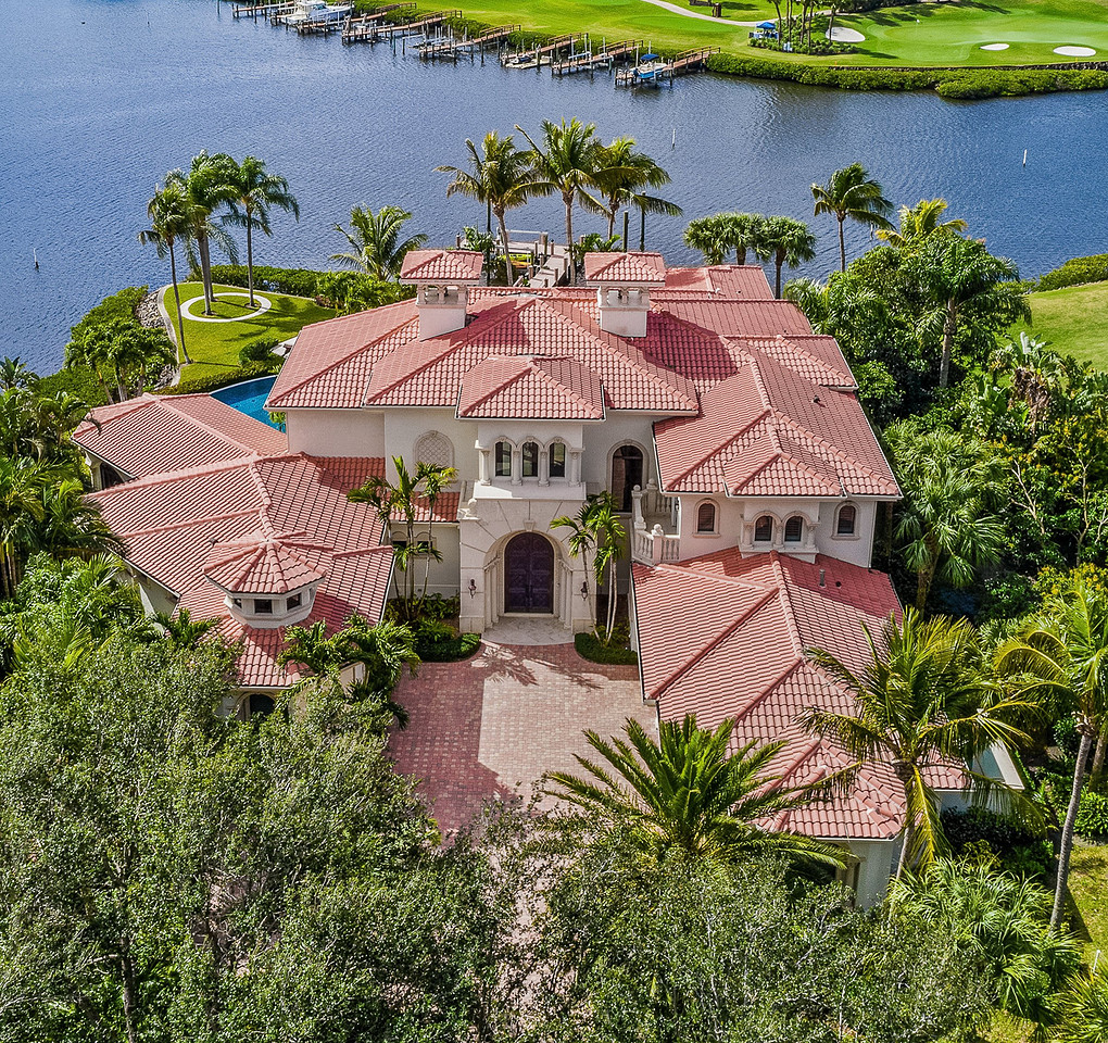 Aerial drone photo of a Mediterranean-style waterfront estate with boat docks and golf course in Florida